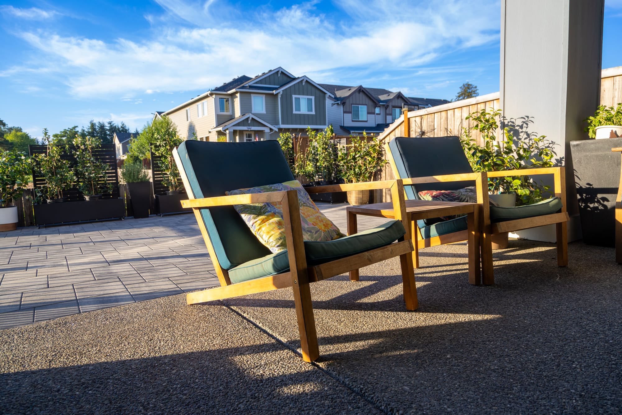 Wood lounge chairs on the finished upper paver patio in golden evening light, with planted privacy screens and a cedar fence beyond