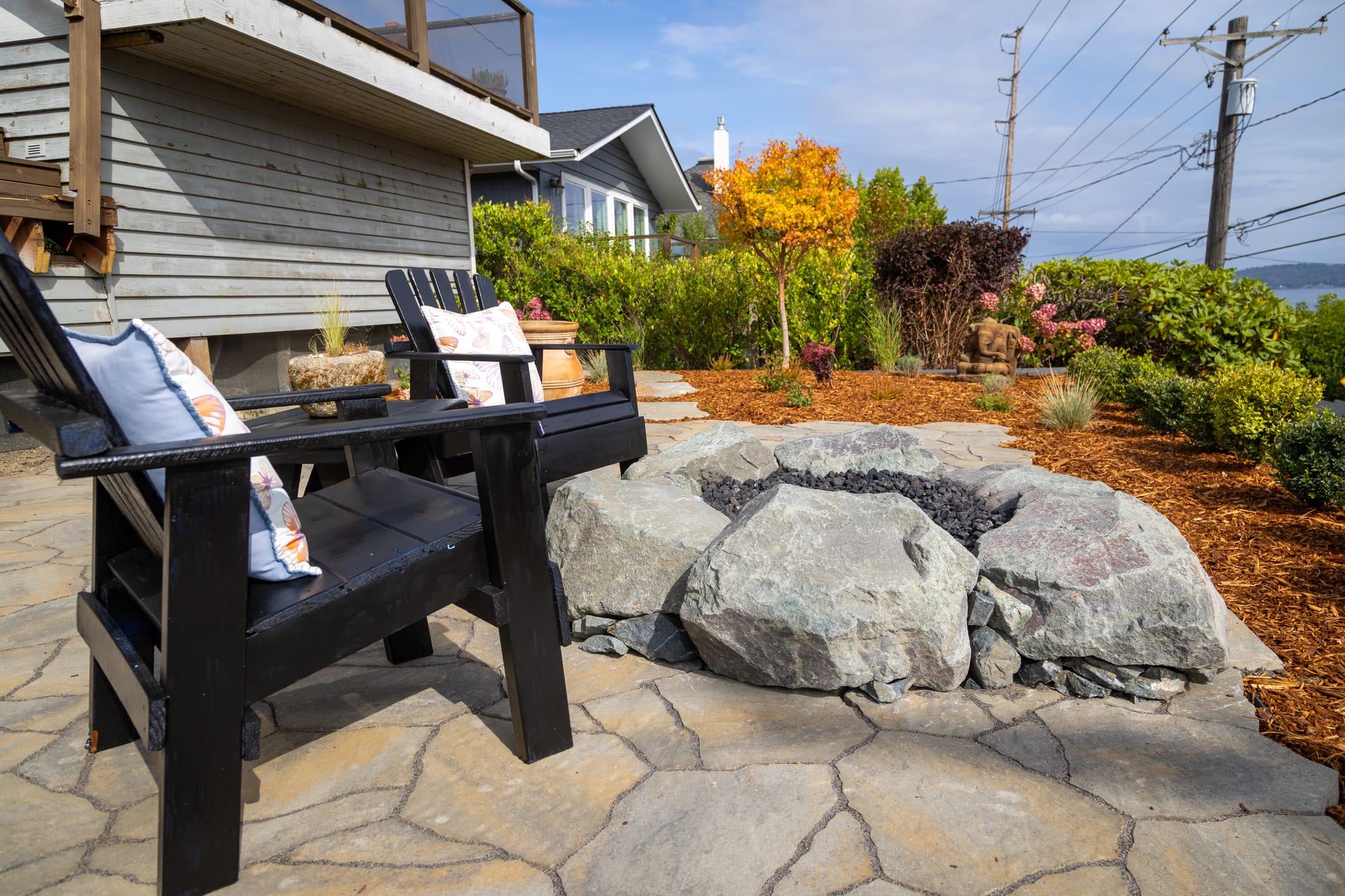 A close view of the boulder fire pit and chairs on the patio, beside the house