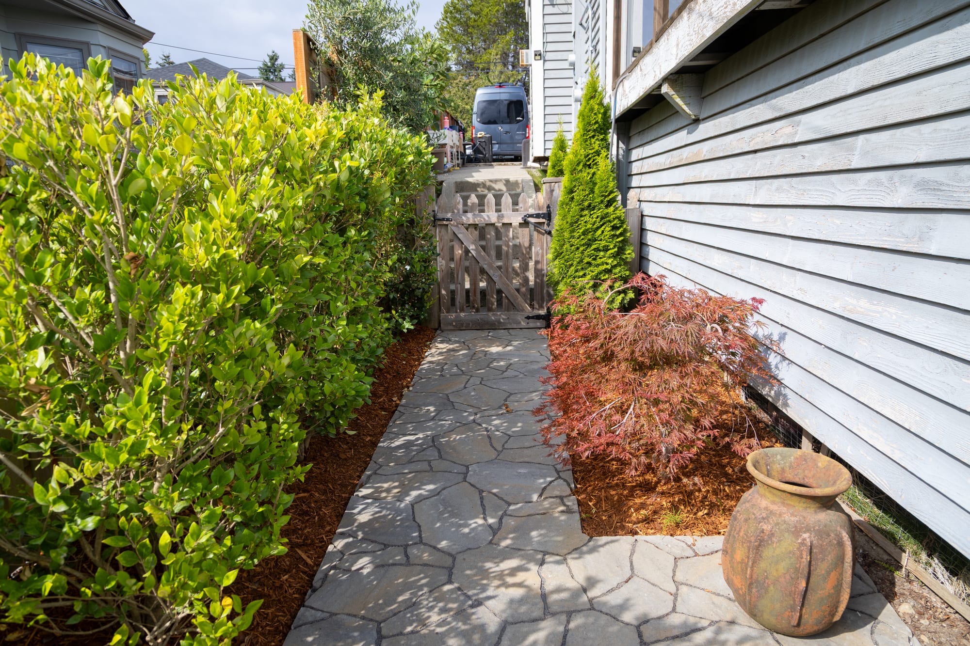 A narrow paver path running along the side of the house to a wood gate