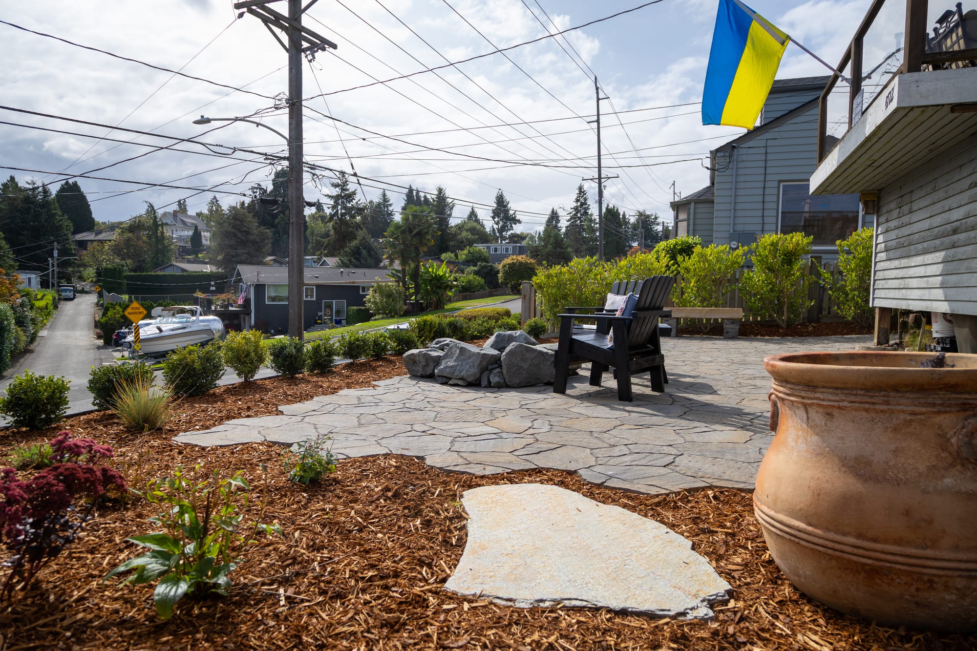 Flat stepping stones through a mulched planting bed toward the patio, with a large terracotta pot in the foreground