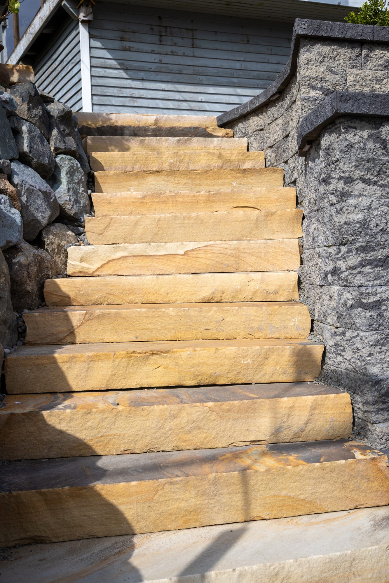 Looking up the stone slab steps between large boulders and a curved retaining wall